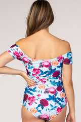 woman wearing a floral off-shoulder maternity swimsuit, showing the back view with colorful flowers on a light blue background