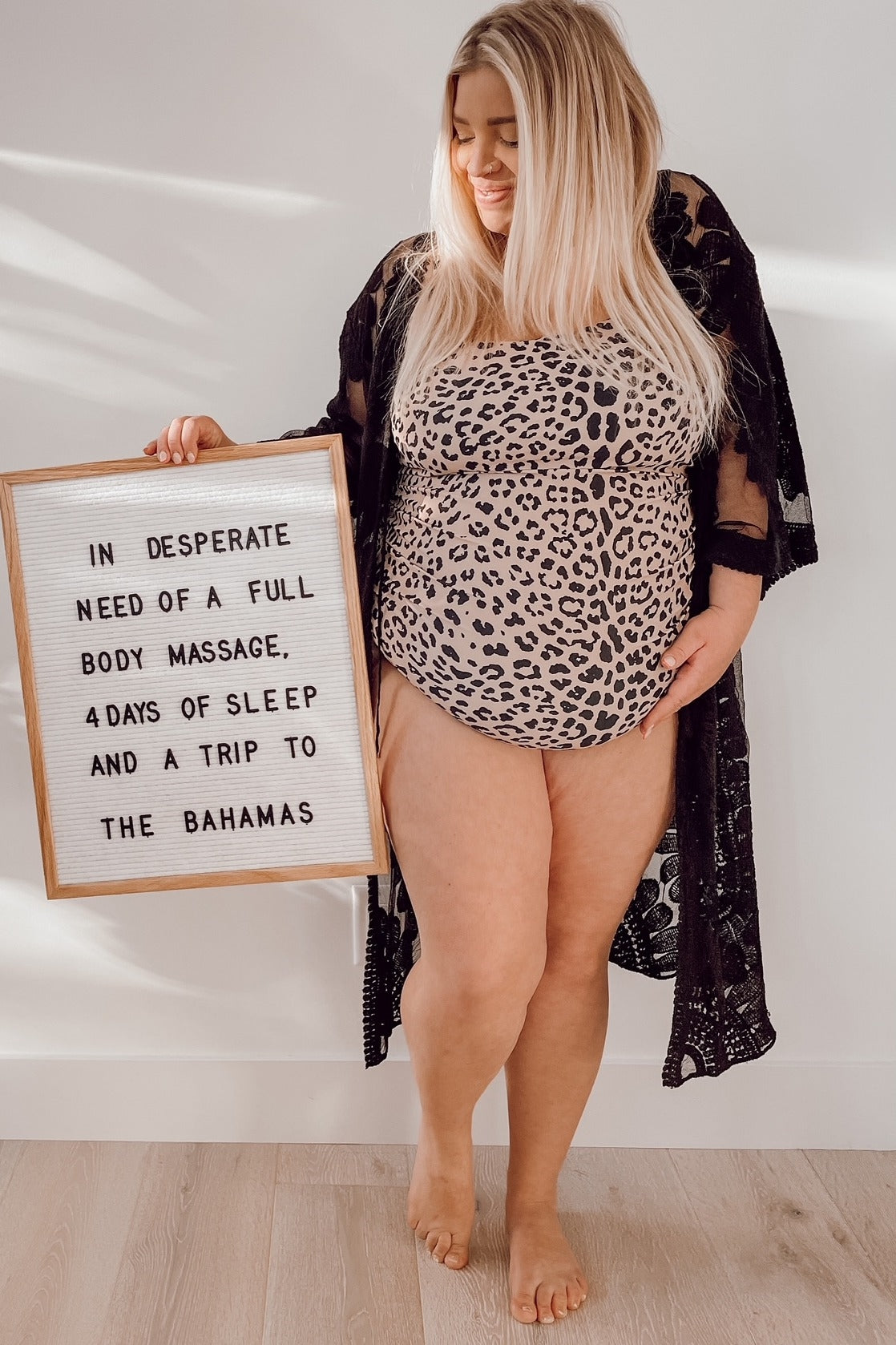 woman wearing a leopard print maternity top and black lace kimono, holding a sign about needing a massage and vacation