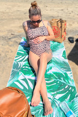 woman wearing a leopard print maternity swimsuit, relaxing on a beach towel with a visible baby bump