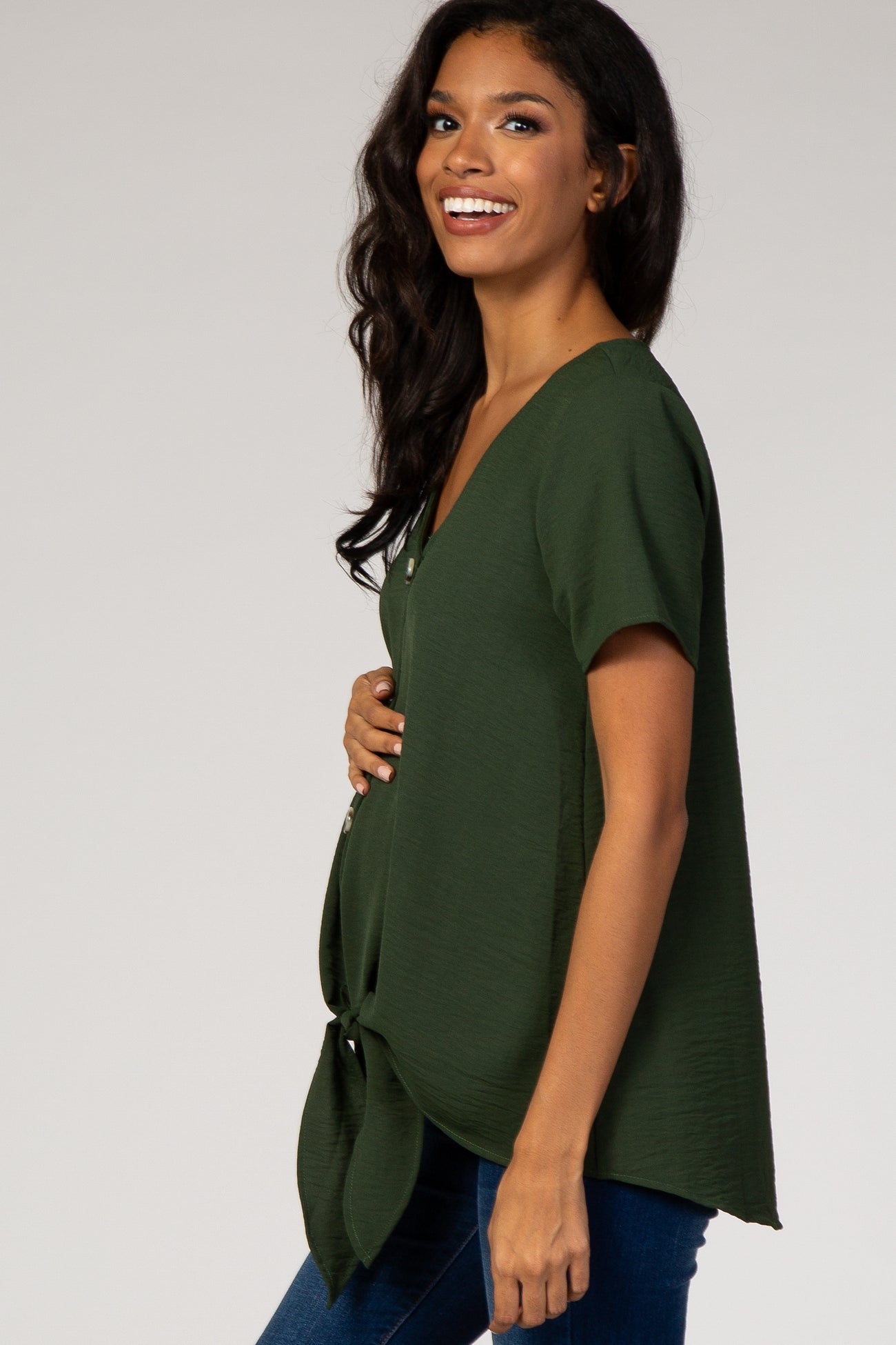 Smiling pregnant woman wearing a forest green short sleeve maternity top with a front tie detail