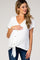 woman wearing a white short sleeve maternity top with a tie front and button details, gently holding her baby bump