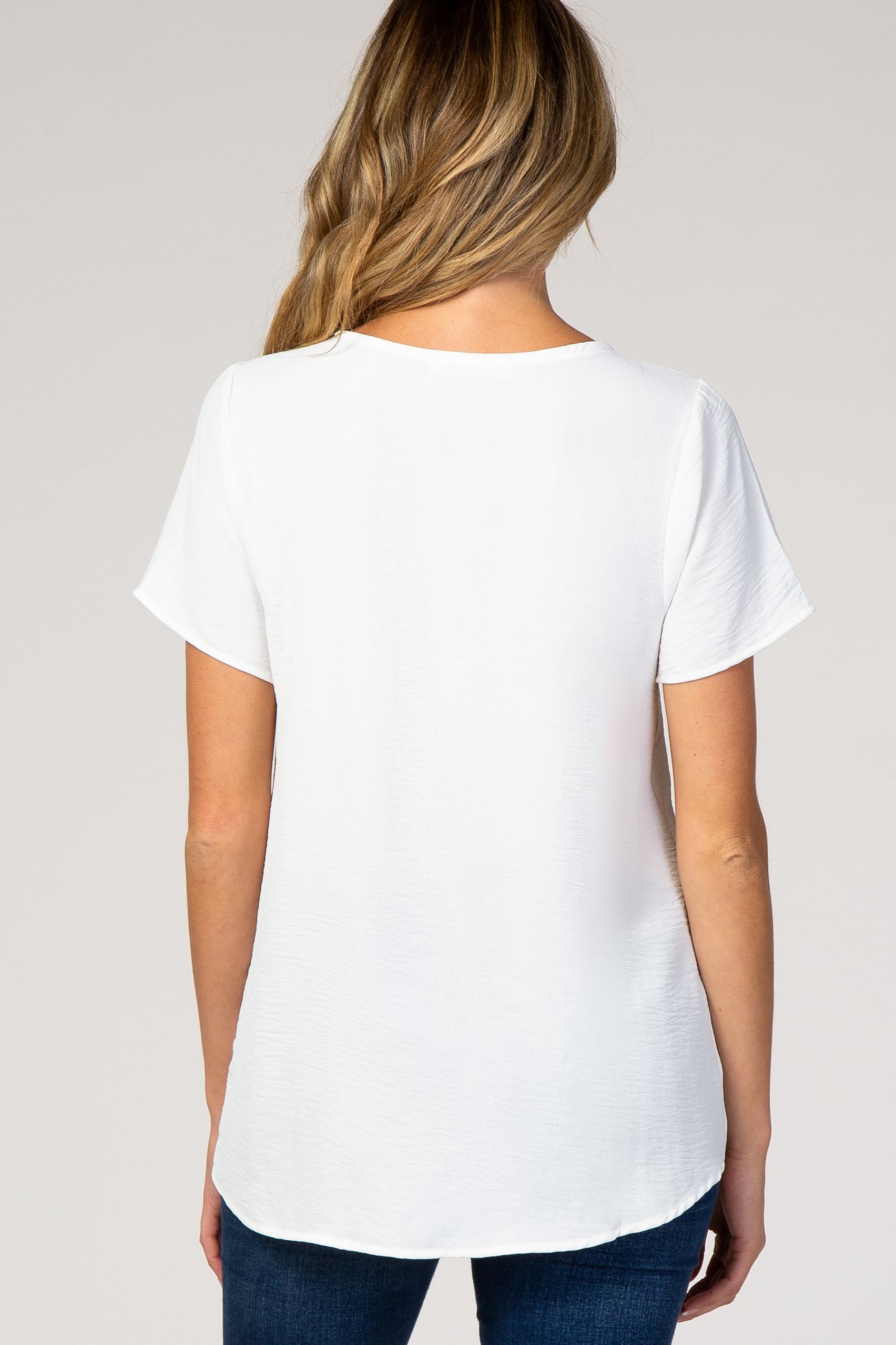 woman wearing a white short sleeve maternity top, view from the back, paired with dark blue jeans