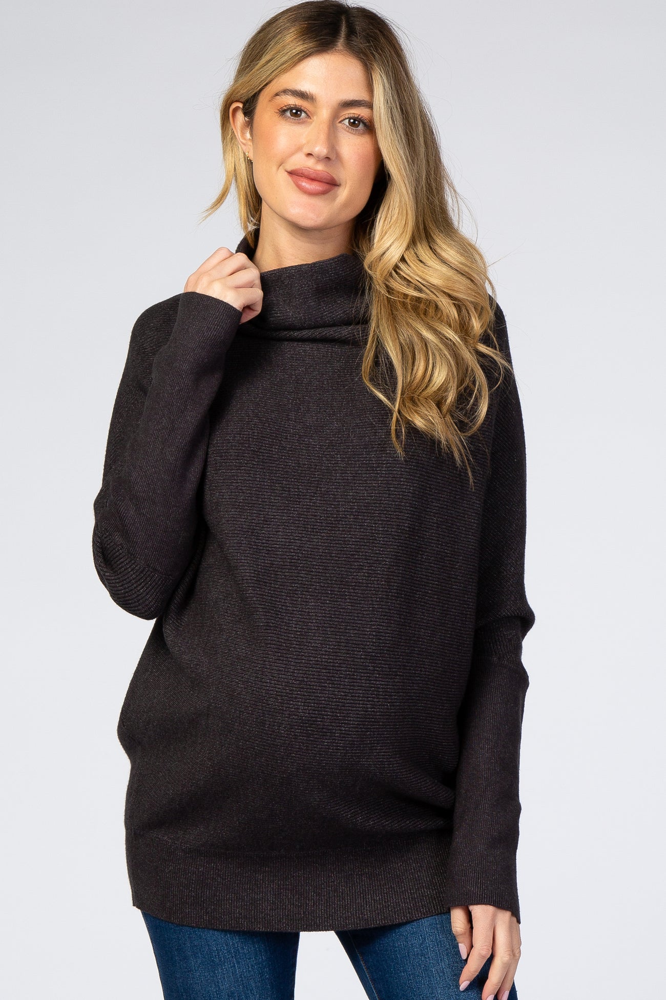 woman wearing a dark gray maternity turtleneck sweater and showing her baby bump while smiling
