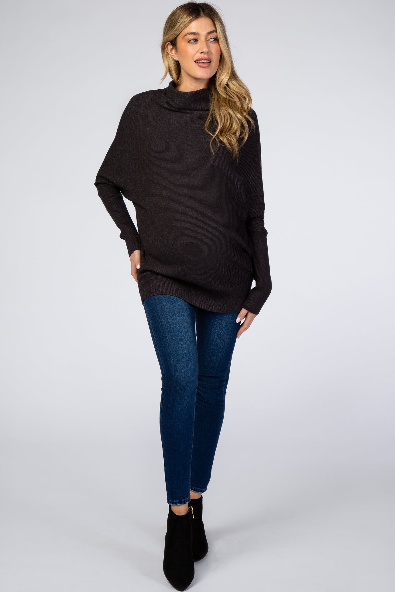 woman wearing a dark gray maternity poncho with a cowl neck and blue skinny jeans, showcasing her baby bump