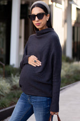 woman wearing a dark gray maternity turtleneck sweater and holding her baby bump outside in casual attire