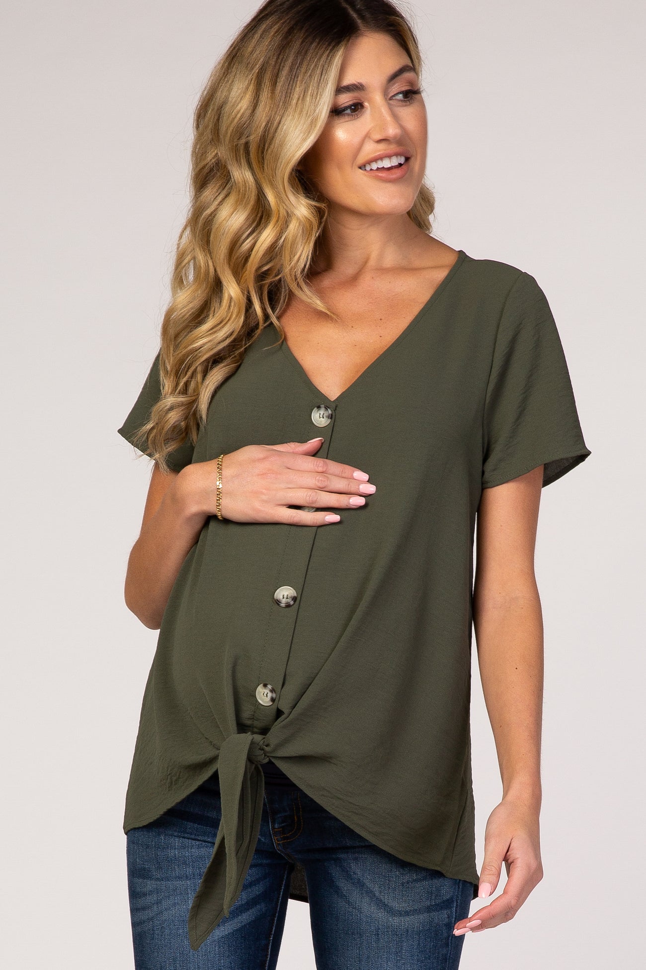 woman wearing an olive green short sleeve maternity top with a v-neck and button details, holding her baby bump