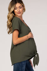 woman wearing an olive green maternity top with a tie detail at the waist and a visible baby bump