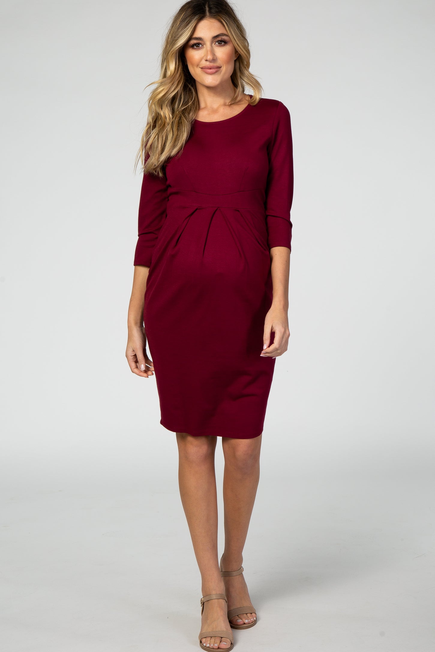 woman wearing a burgundy maternity dress with three-quarter sleeves and a pleated front detail, showing a baby bump