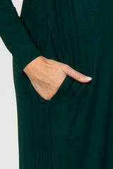 close-up of a woman's hand in the pocket of a dark green maternity dress with long sleeves