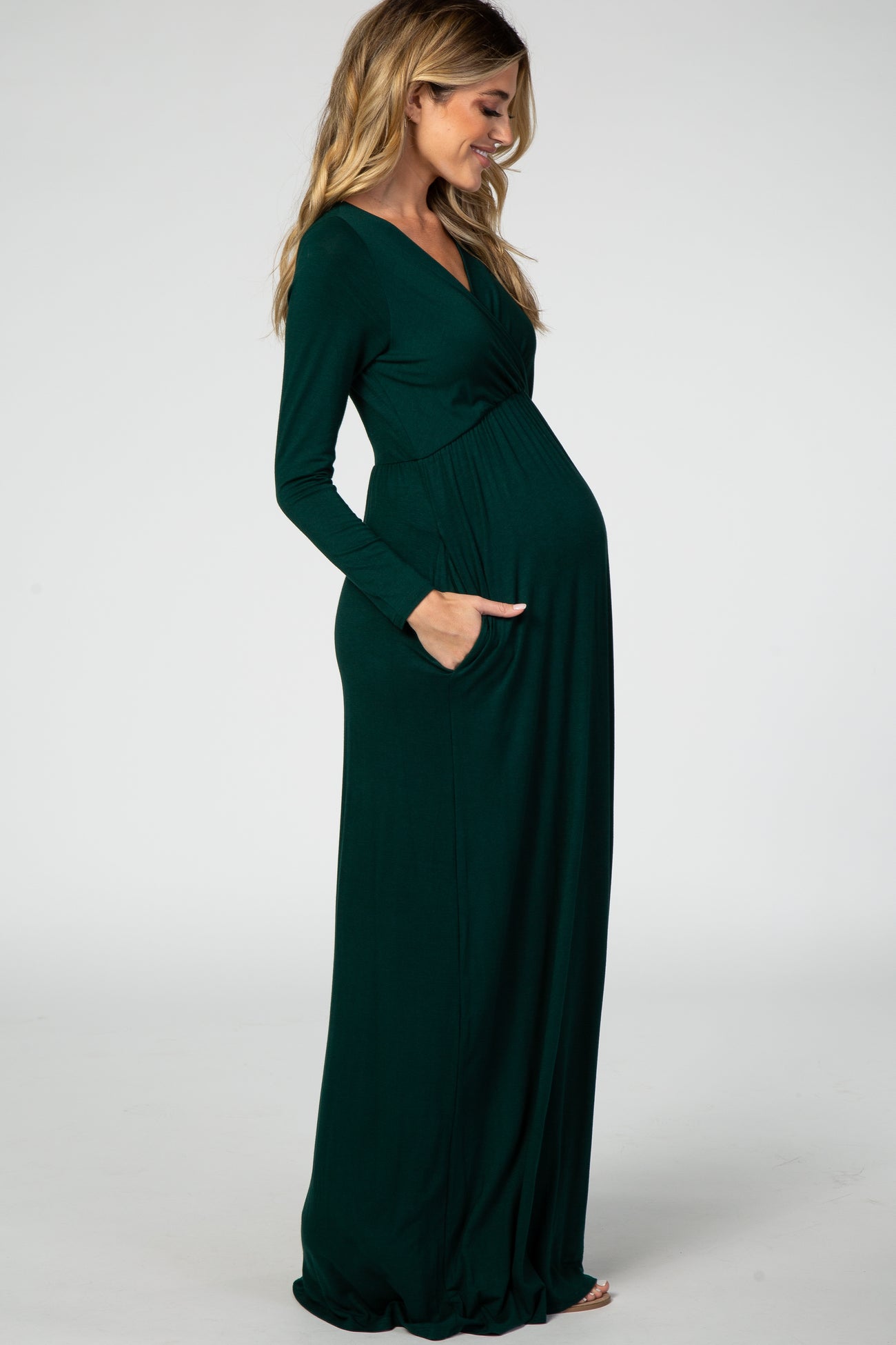 woman wearing a dark green long sleeve maternity maxi dress with pockets and a visible baby bump