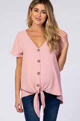 woman wearing a pink maternity top with a v-neck, button details, and a front tie, styled with dark jeans