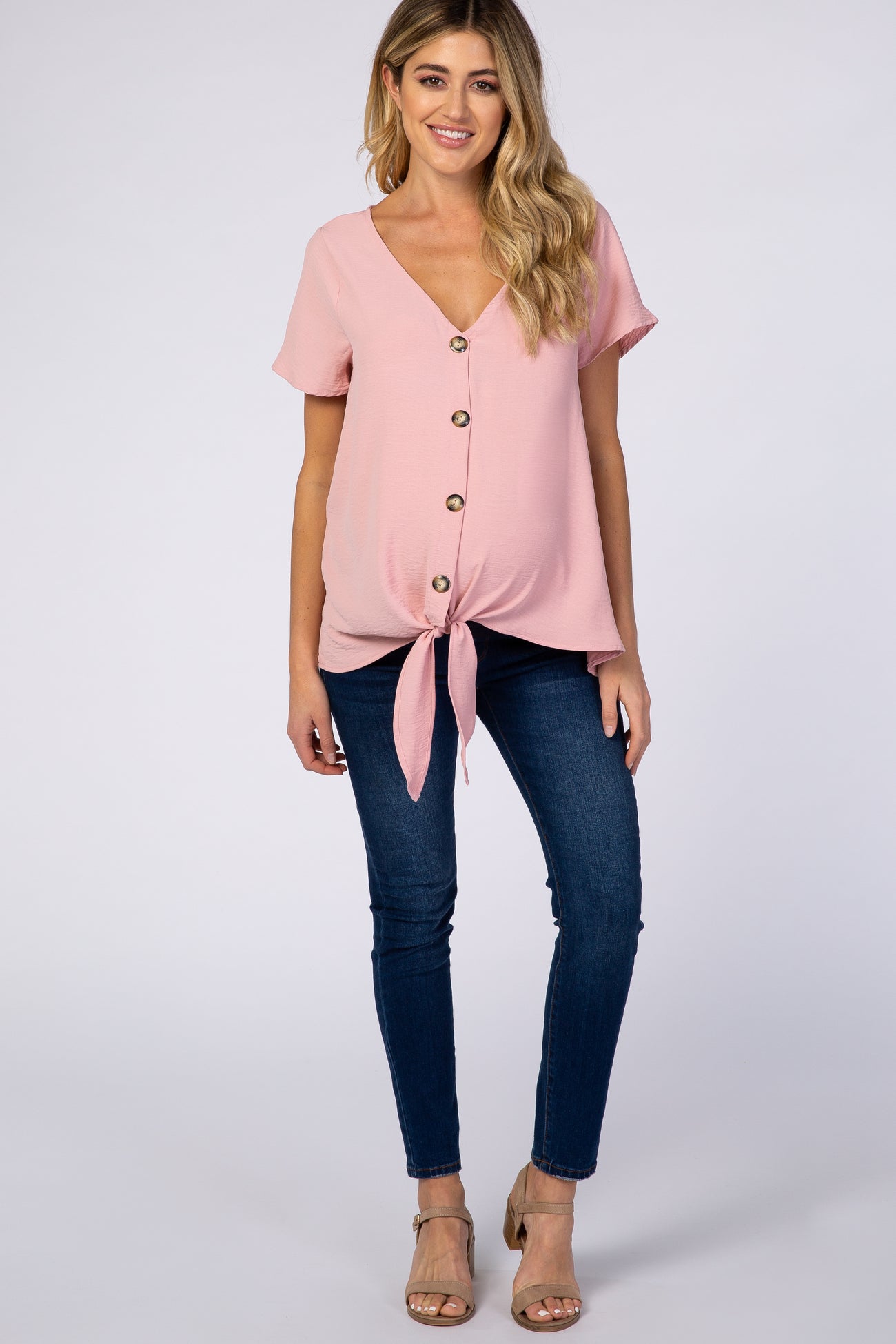 woman wearing a light pink maternity top with buttons and a front tie, paired with dark skinny jeans