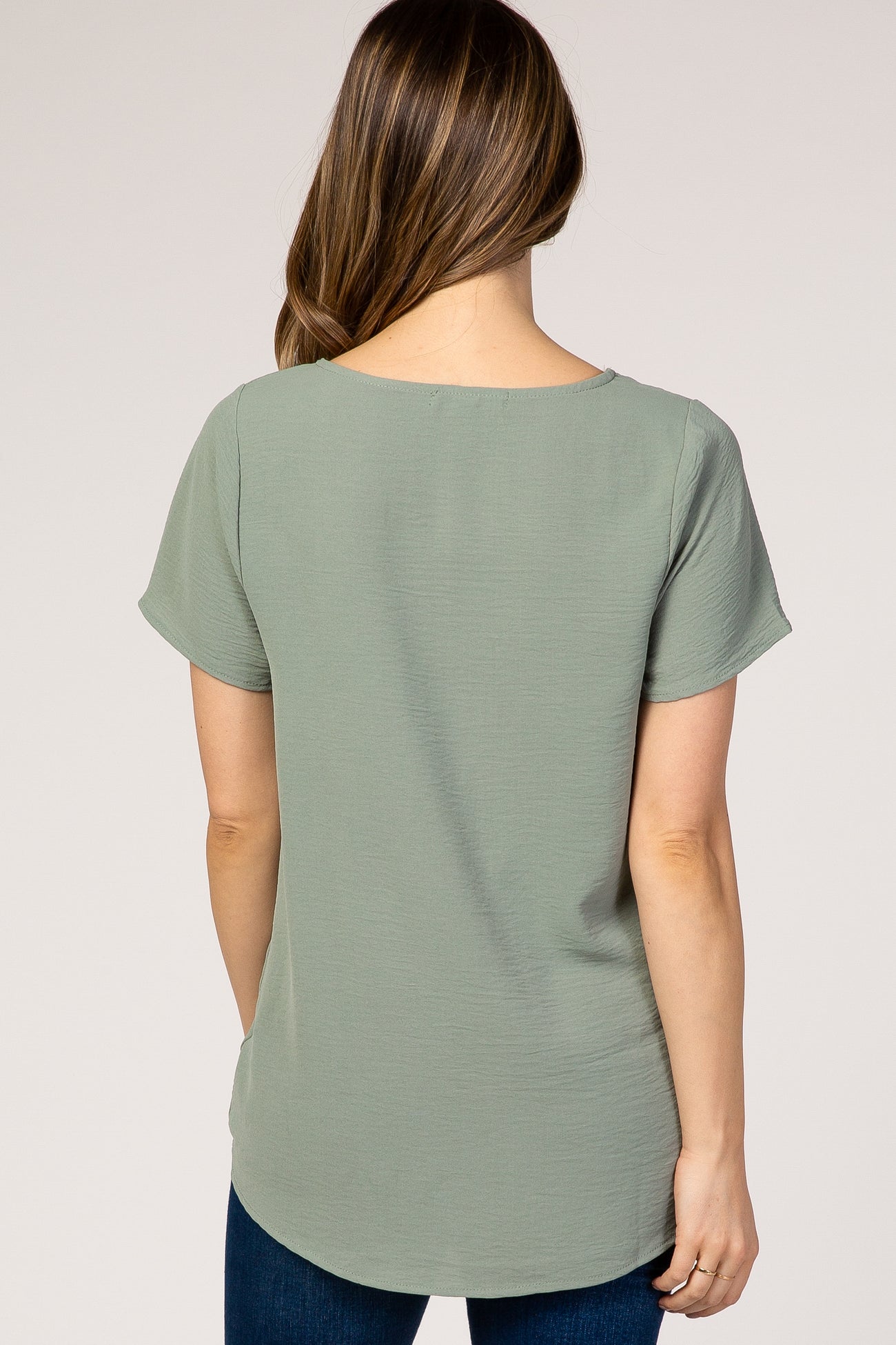 woman wearing a light green short sleeve maternity top, viewed from the back with a relaxed fit
