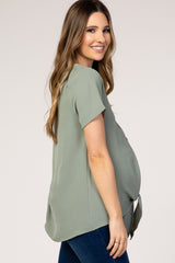 woman wearing a sage green short sleeve maternity top with a tied hem and visible baby bump