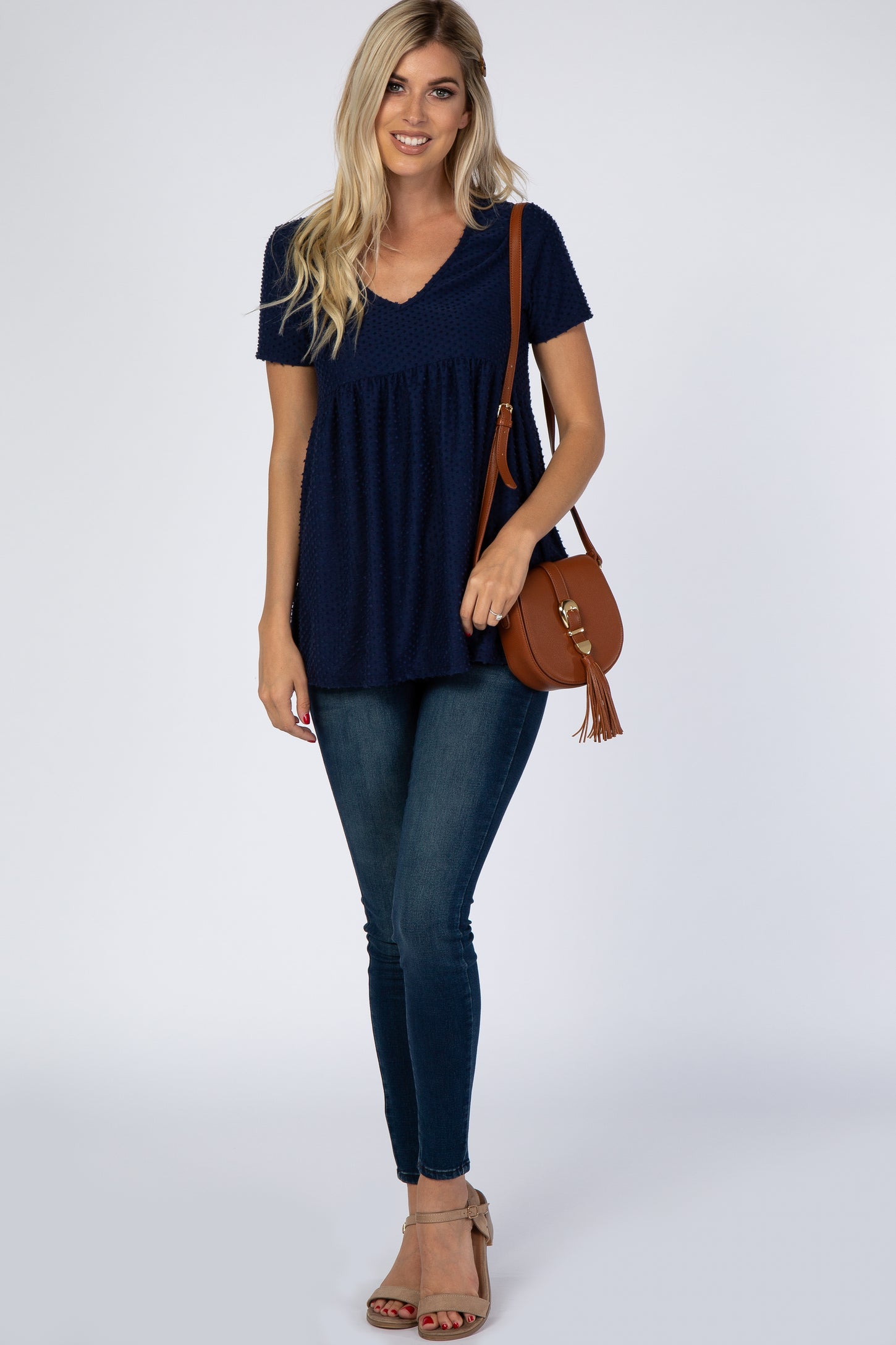 woman wearing a navy blue short sleeve peplum top paired with skinny jeans and a brown crossbody bag