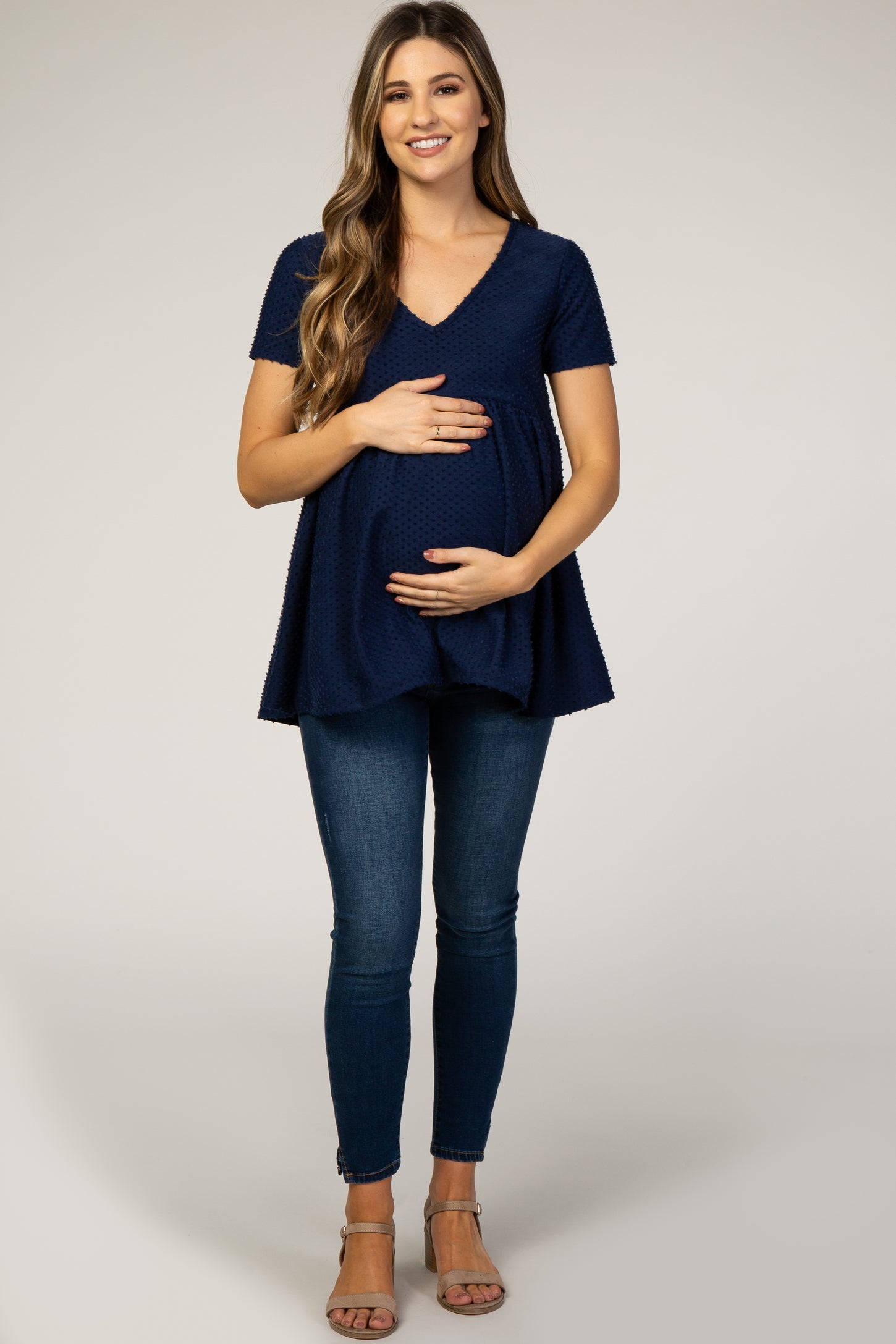 woman wearing a navy short sleeve maternity top with a v-neck and holding her baby bump, paired with skinny jeans