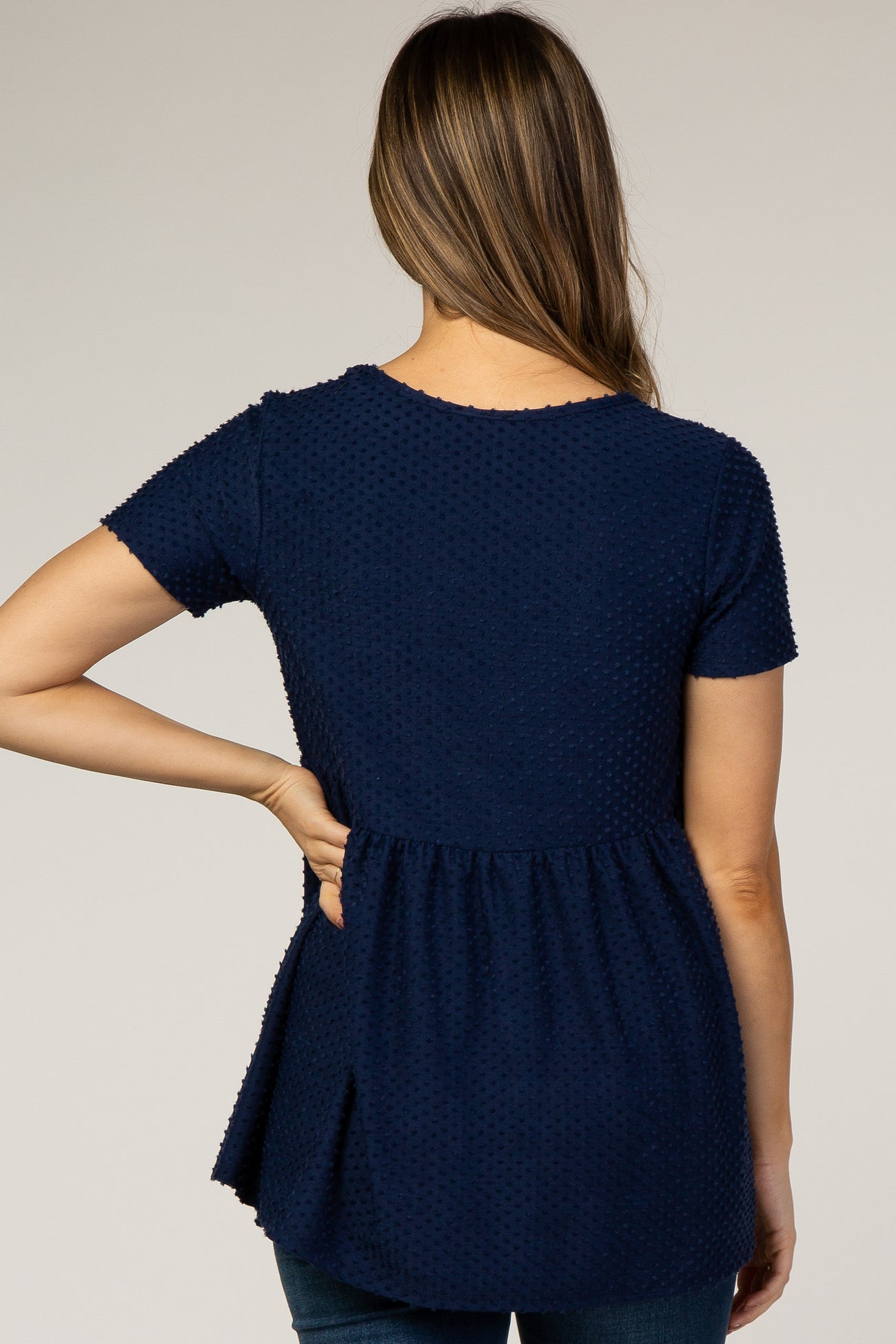 woman wearing a navy blue short sleeve maternity top with textured details and a peplum hem, showing her back