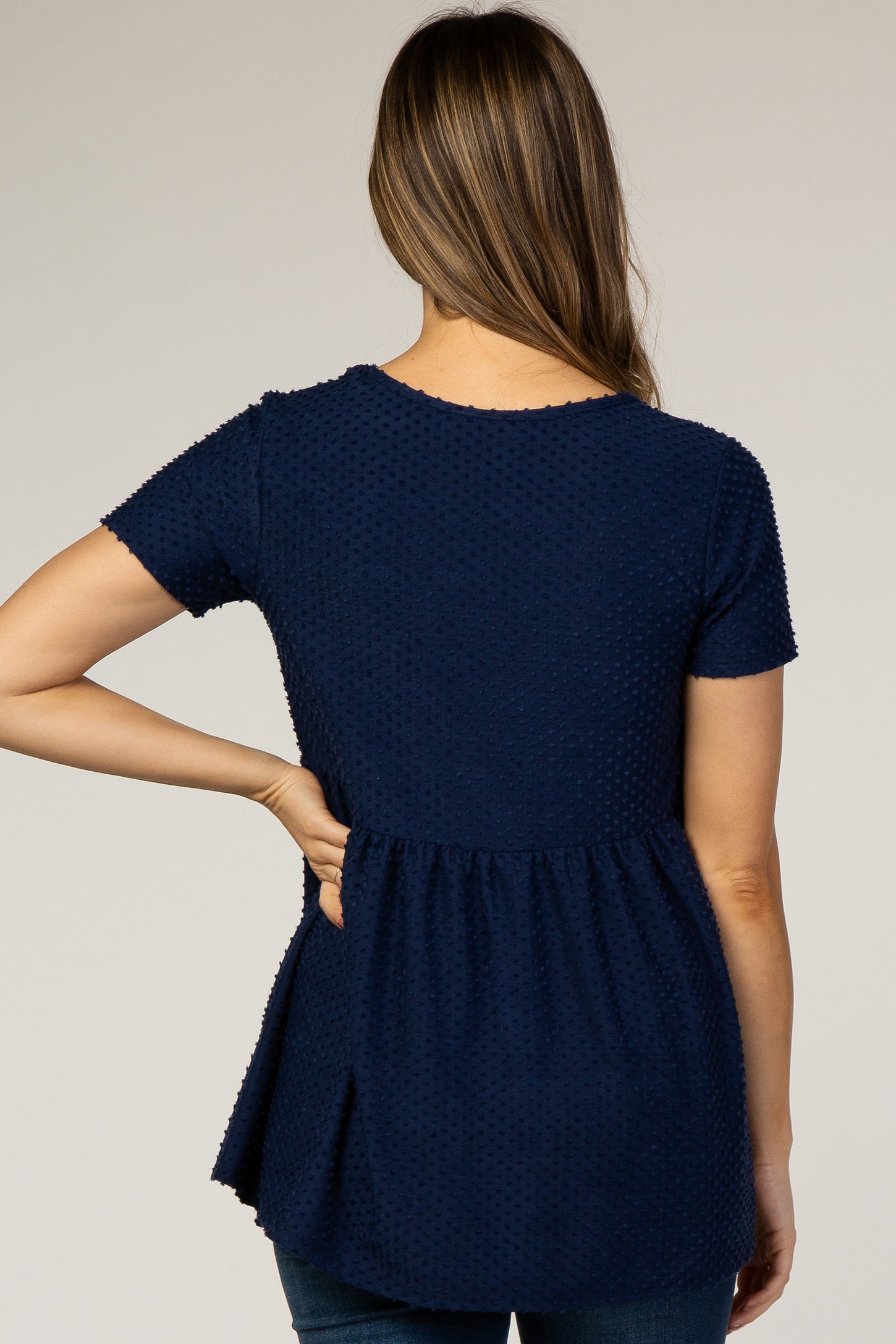 woman wearing a navy blue short sleeve maternity top with textured details and a peplum hem, showing her back