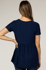 woman wearing a navy blue short sleeve maternity top with textured details and a peplum hem, showing her back
