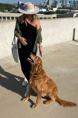 woman wearing a black maternity dress and green cardigan, standing with a golden retriever on a rooftop