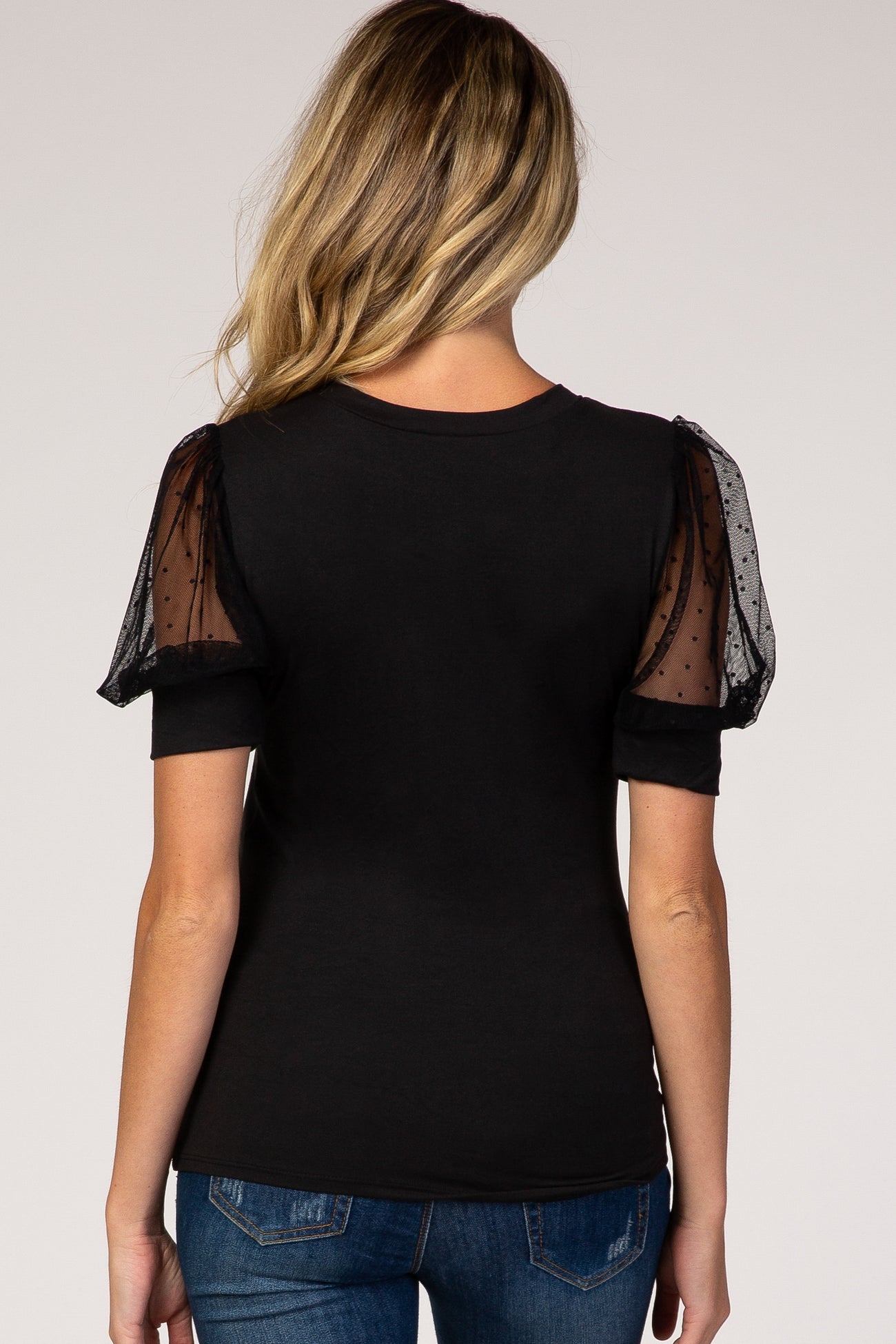 woman wearing a black maternity top with sheer polka dot puff sleeves and a curved hem, showing her back