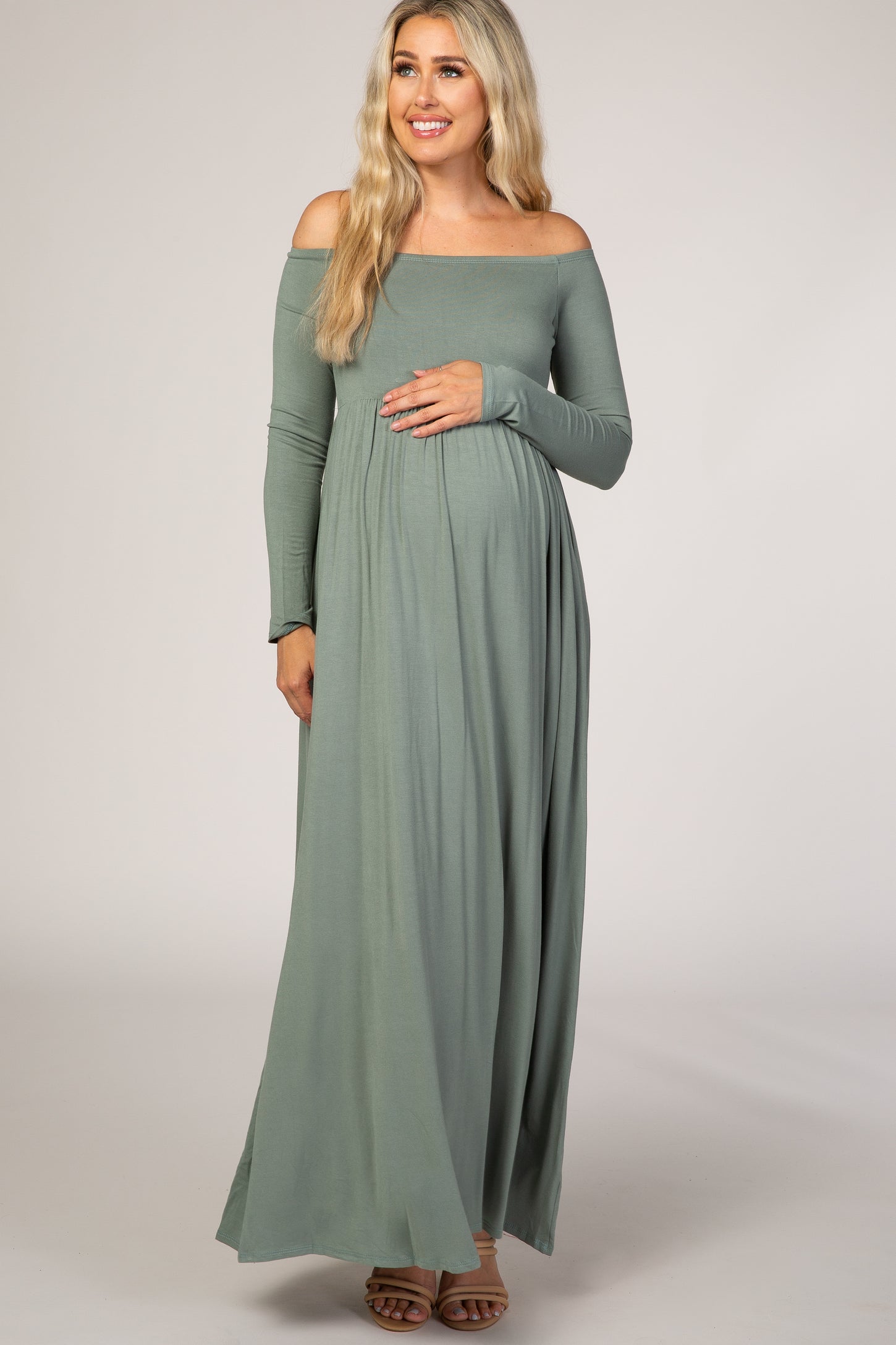 woman wearing a sage green off-the-shoulder maternity maxi dress and holding her baby bump