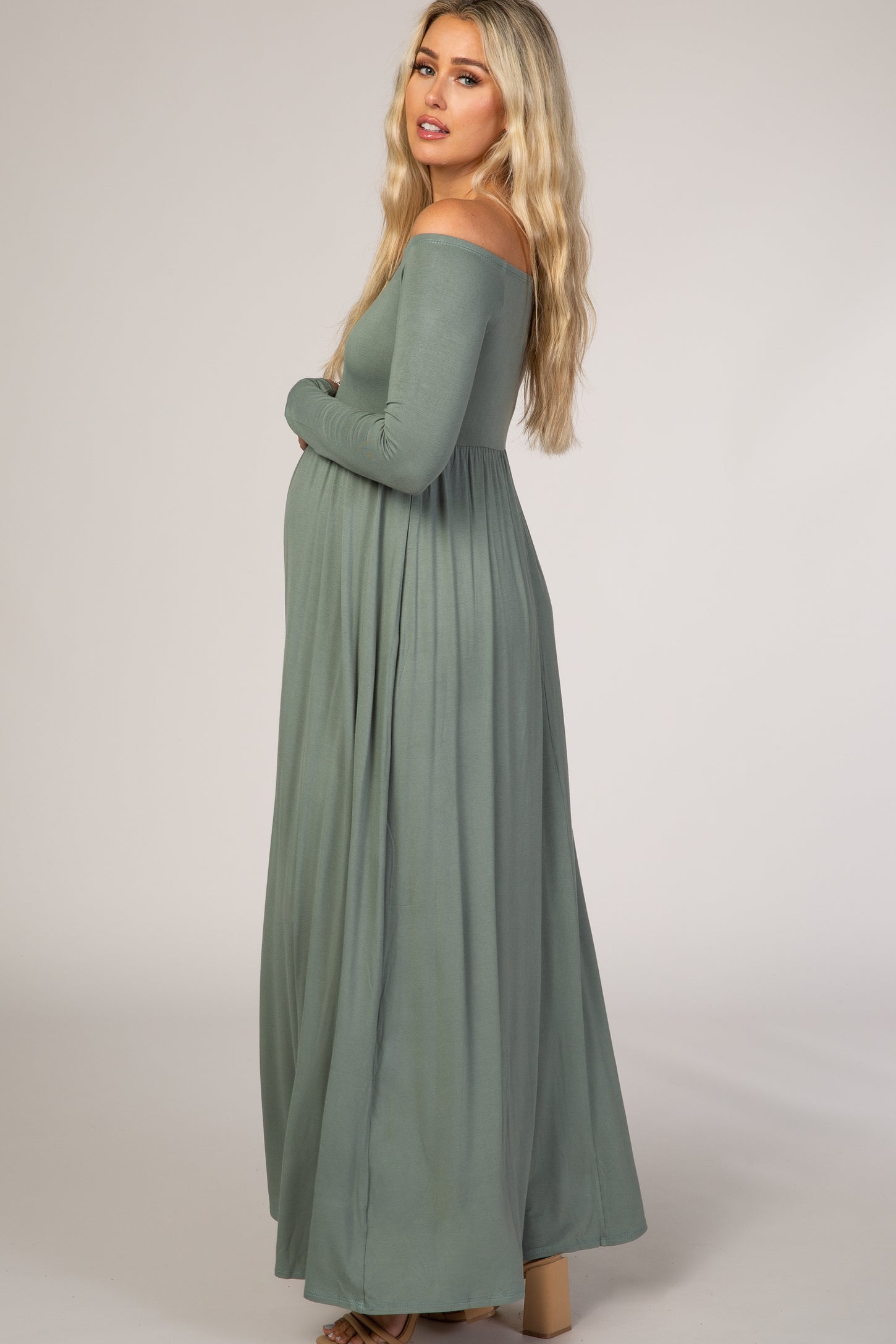 woman wearing a sage green off-shoulder maternity maxi dress with a flowing skirt and visible baby bump