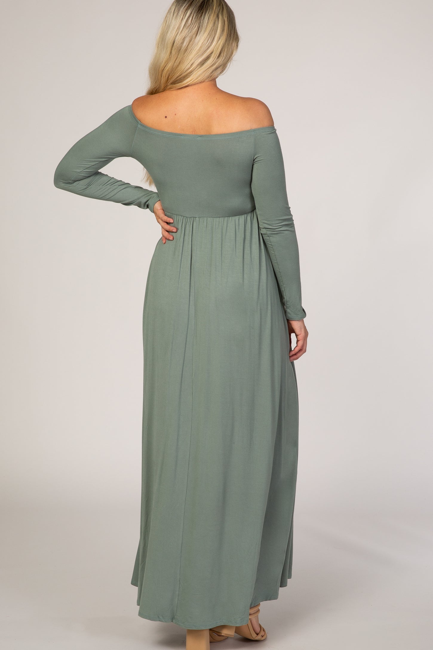 woman wearing a sage green off-shoulder maxi maternity dress with a fitted bodice and flowing skirt, seen from the back