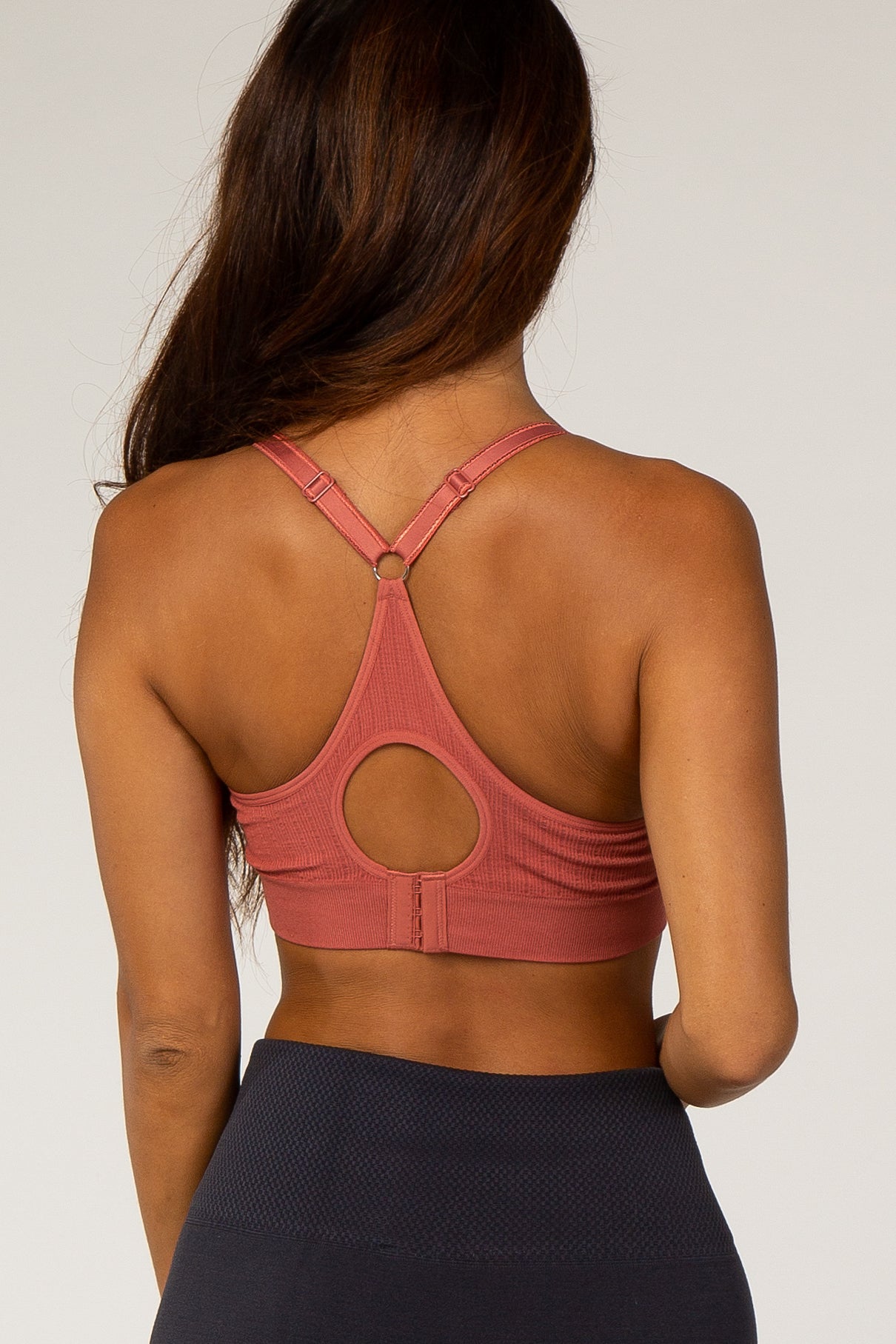 woman wearing a rose pink sports bra with a round cutout back and crisscross straps