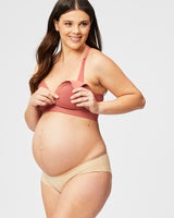 woman wearing a rust-colored maternity bra and nude maternity briefs, holding open the bra to show her baby bump