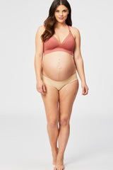 woman wearing a rust-colored lace bralette and nude maternity bikini underwear, showing her baby bump