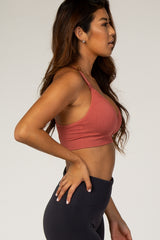 woman wearing a rust-colored ribbed sports bra, showing a side profile with hair down and leggings visible