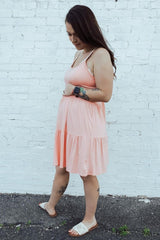 woman wearing a light pink maternity dress with tiered layers and holding her baby bump