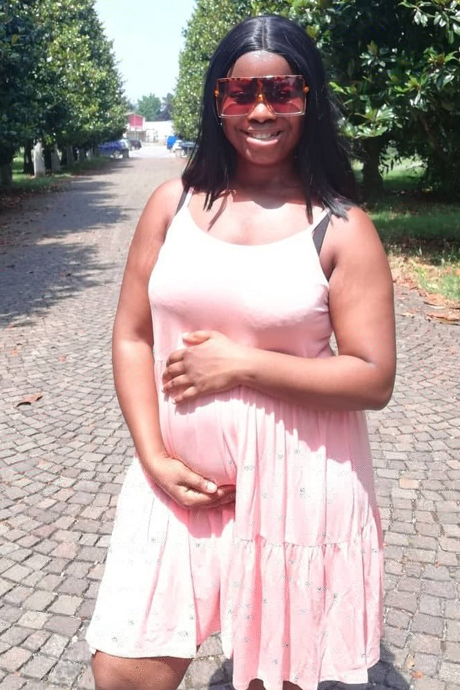 woman wearing a light pink maternity dress with a ruffled hem and holding her baby bump
