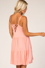 woman wearing a coral sleeveless dress with a tiered design and a lace-up back detail