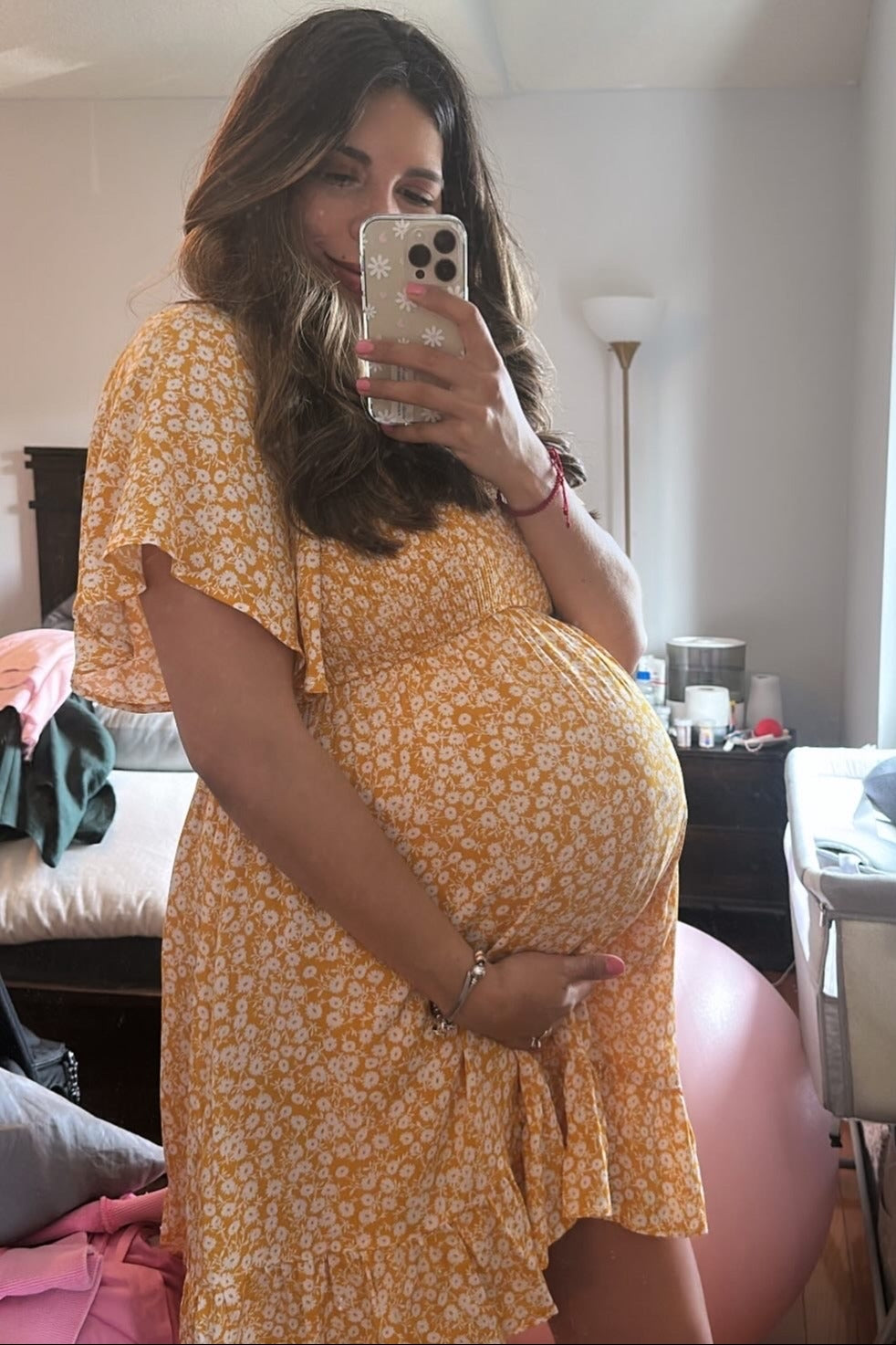woman wearing a yellow floral maternity dress and holding her baby bump