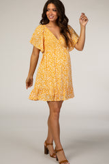 woman wearing a yellow floral maternity dress with short flutter sleeves and a relaxed fit, smiling and posing