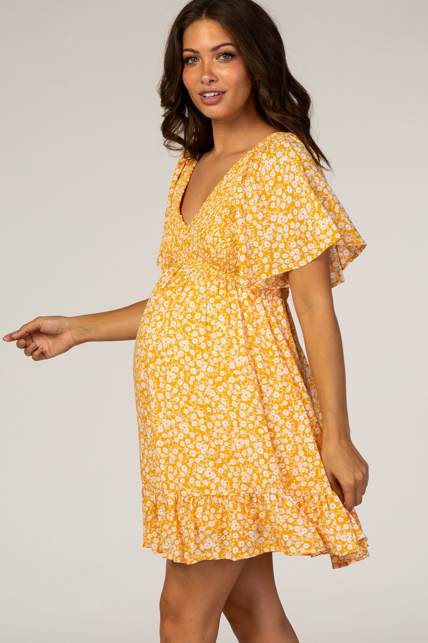 woman wearing a yellow floral maternity dress with flutter sleeves and a baby bump visible