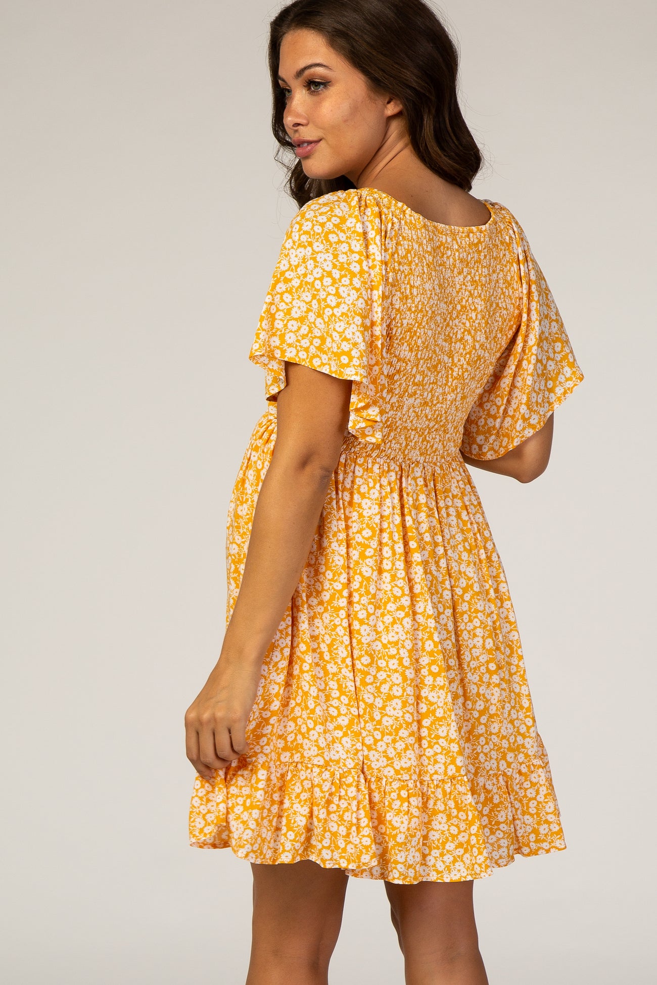 woman wearing a yellow floral maternity dress with short sleeves and a tiered hem, showing her baby bump