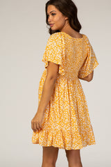 woman wearing a yellow floral maternity dress with short sleeves and a tiered hem, showing her baby bump