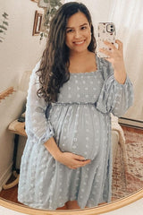 woman wearing a light blue maternity dress with puff sleeves, smiling and holding her baby bump in front of a mirror