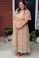 woman wearing a blush floral pleated maternity maxi dress and holding her baby bump