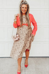 woman wearing a floral maternity dress with a coral blazer and holding a small pink handbag, smiling and showing baby bump