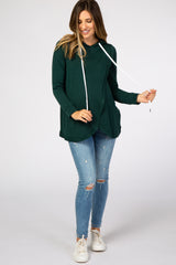 woman wearing a forest green long sleeve nursing hoodie with distressed blue jeans and white sneakers
