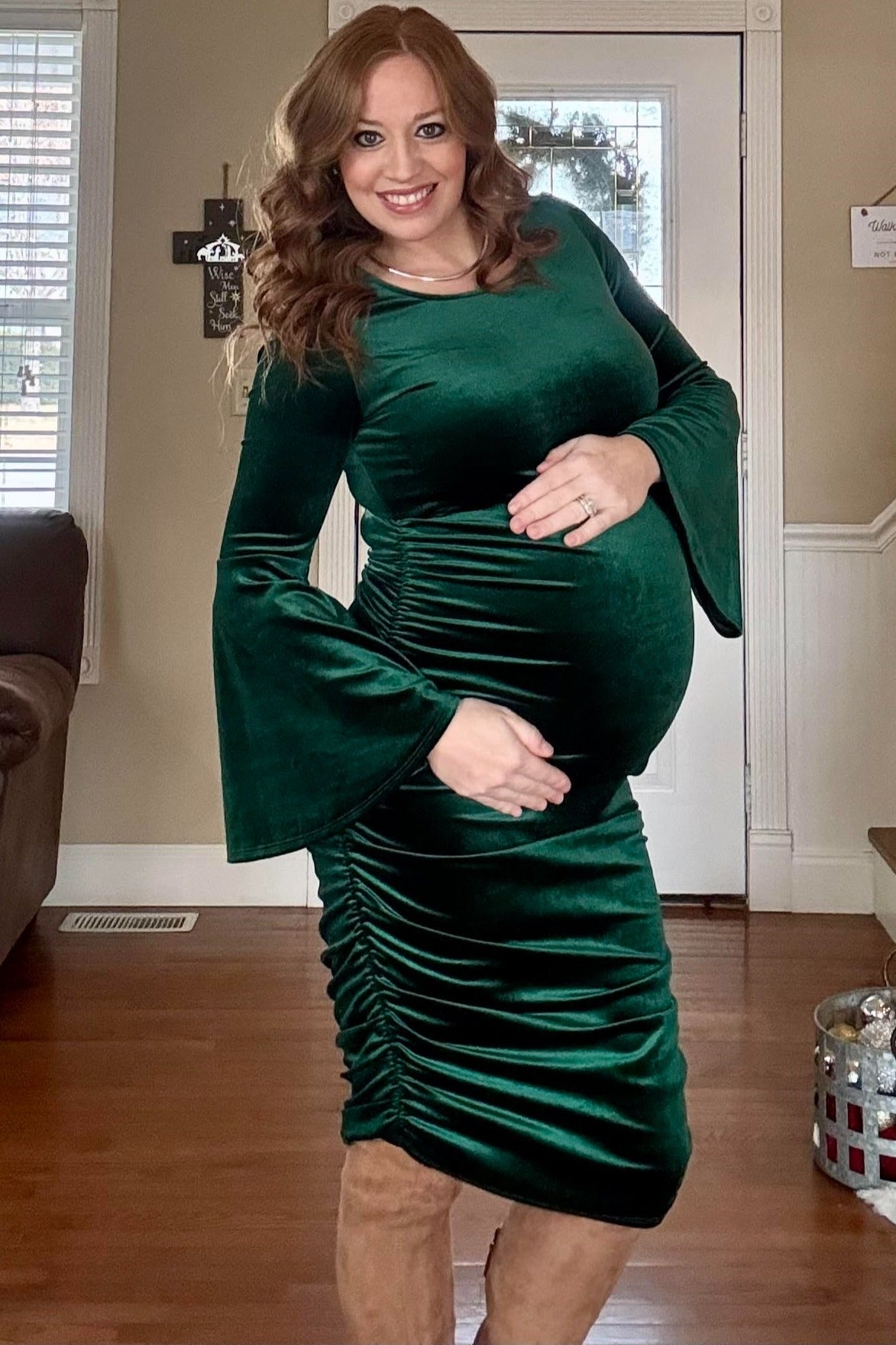 woman wearing a dark green velvet maternity dress with bell sleeves and ruching, showing baby bump