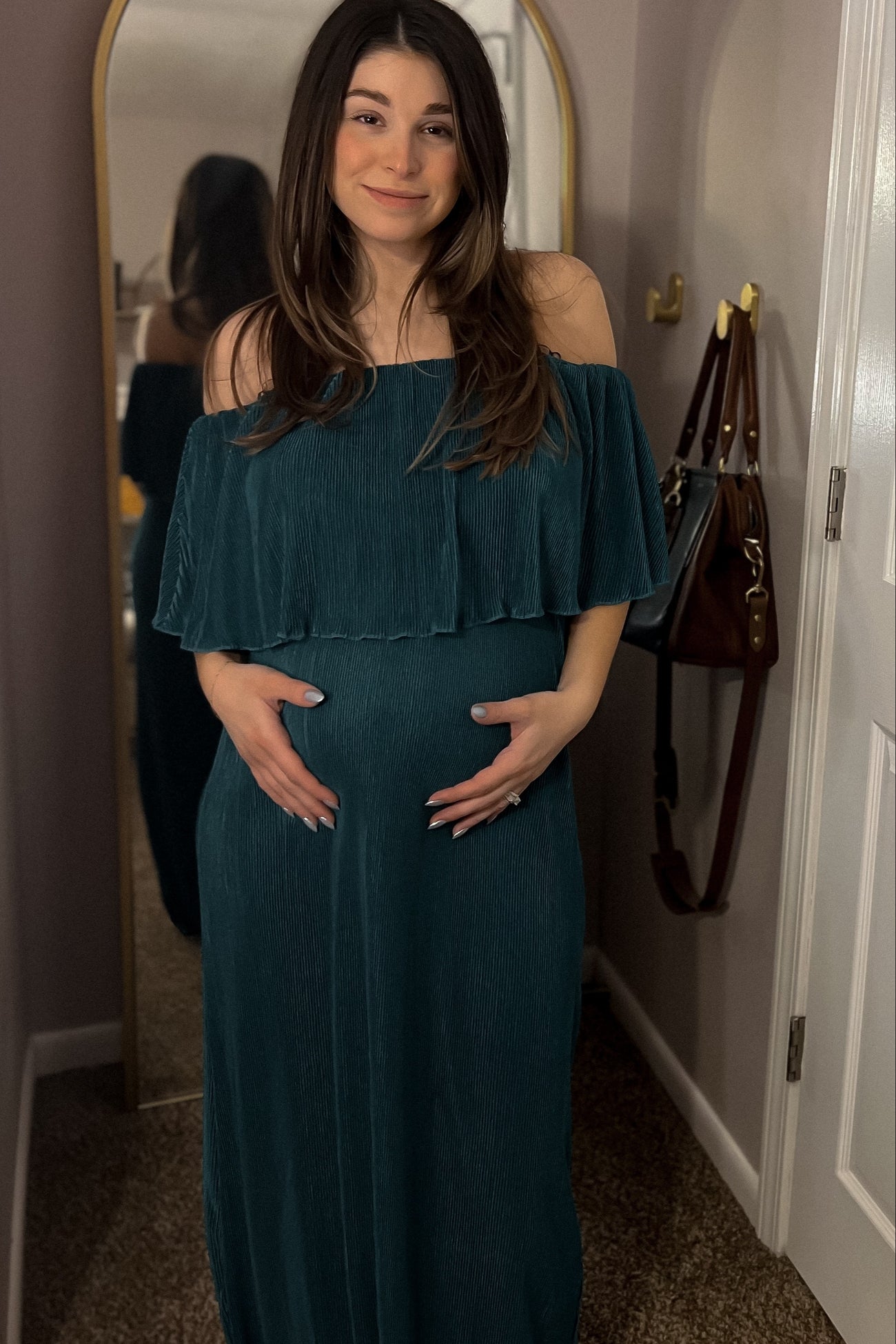 woman wearing a teal off-the-shoulder maternity dress and holding her baby bump