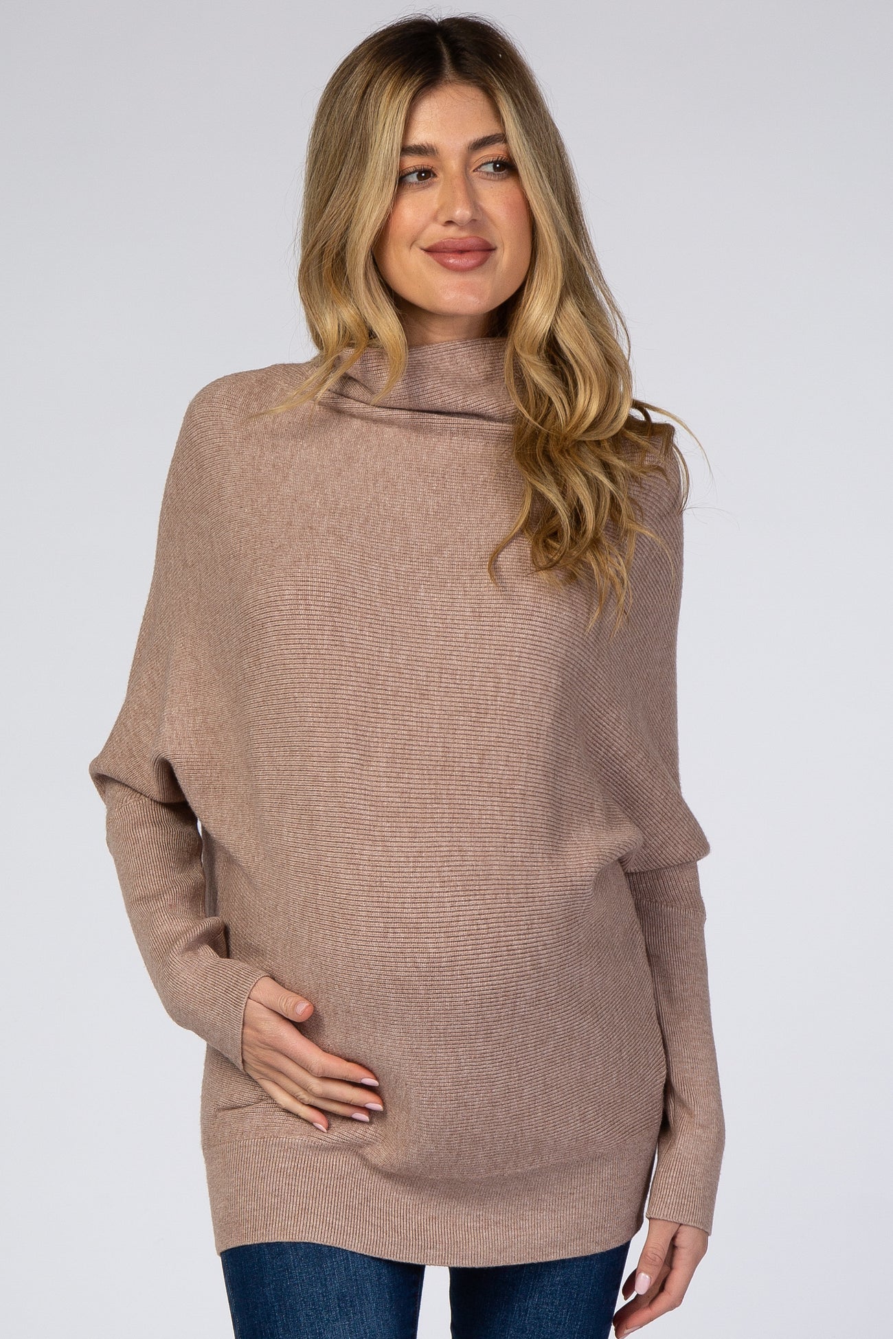 woman wearing a light taupe oversized maternity sweater, gently holding her baby bump
