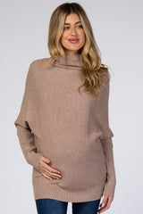 woman wearing a light taupe oversized maternity sweater, gently holding her baby bump