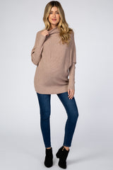 woman wearing a light pink oversized maternity sweater with a cowl neck and blue skinny jeans, showing her baby bump