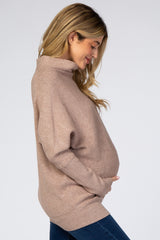 woman wearing a light brown oversized turtleneck maternity sweater and holding her baby bump